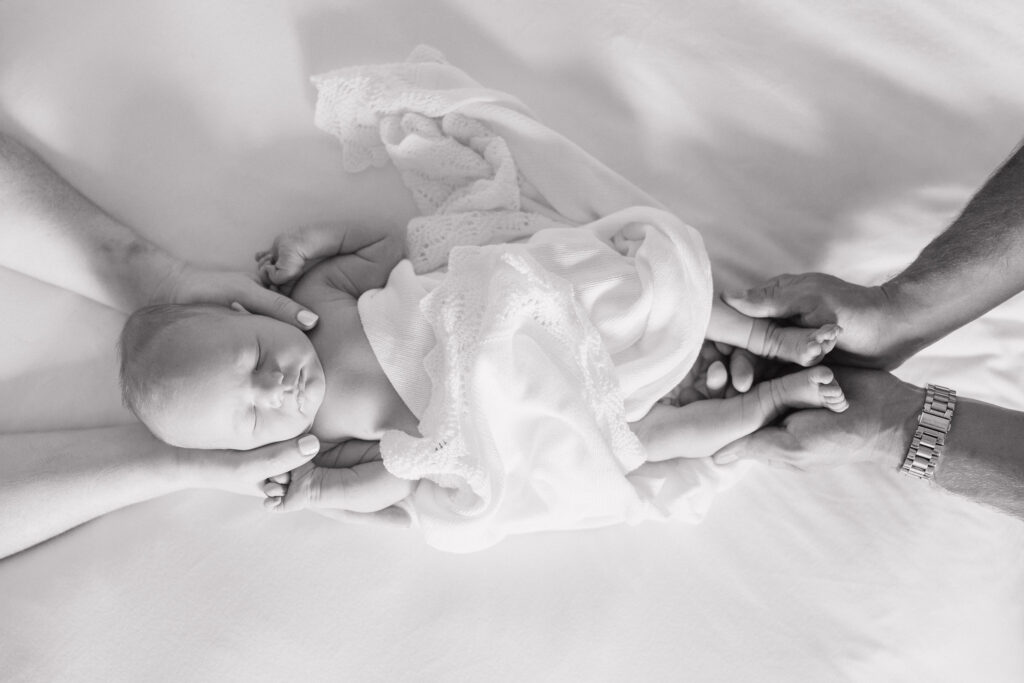 newborn baby resting between mom and dads hands