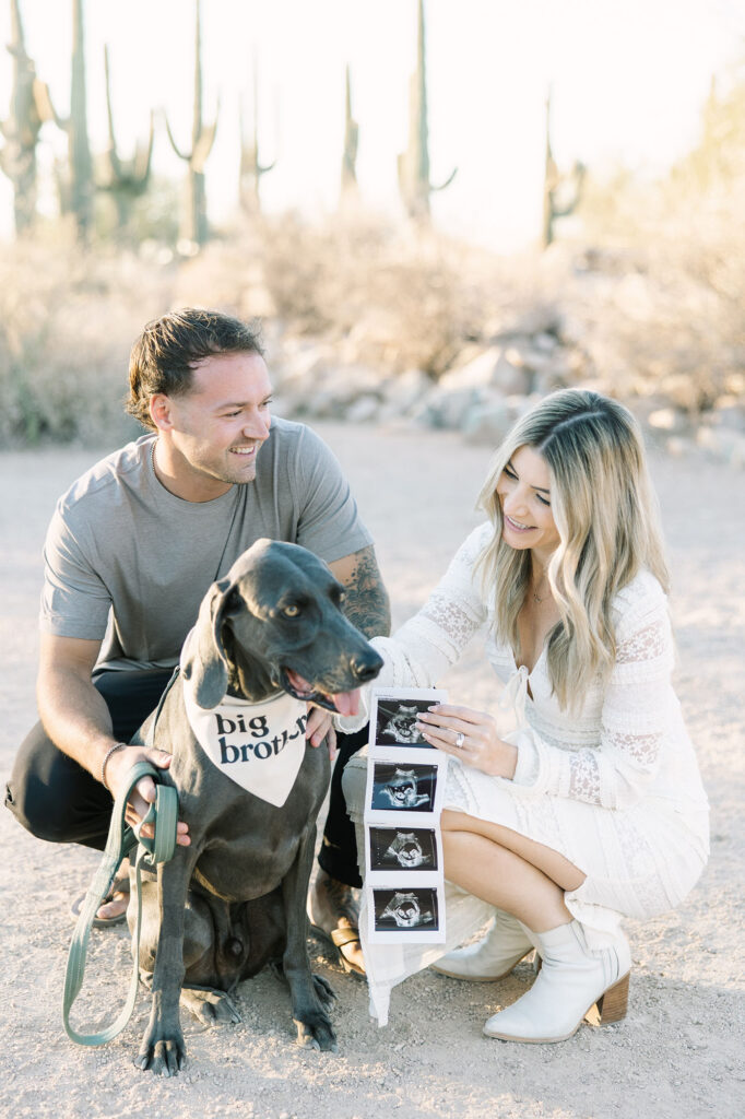 family posing at the Gilbert Riparian Preserve with ultrasound photos announcing their pregnancy.